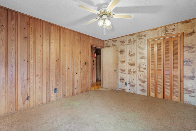 carpeted spare room featuring a ceiling fan, a textured ceiling, and wooden walls