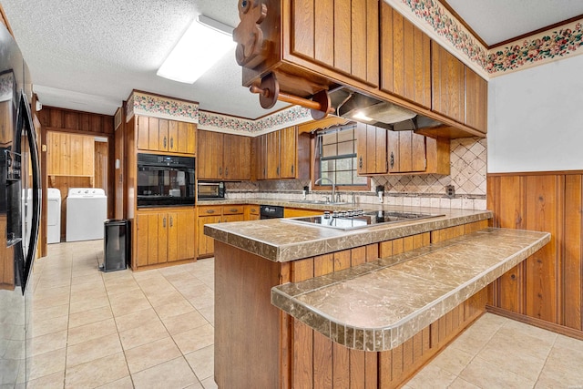 kitchen featuring black appliances, brown cabinetry, a peninsula, and washing machine and dryer