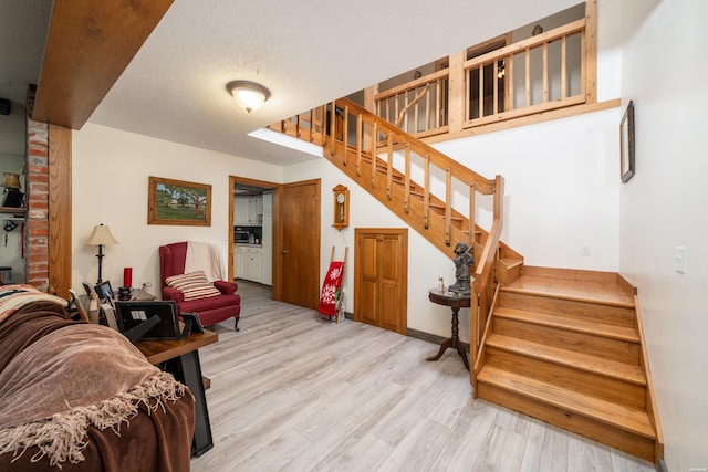 living area with a textured ceiling, stairway, light wood-type flooring, and baseboards