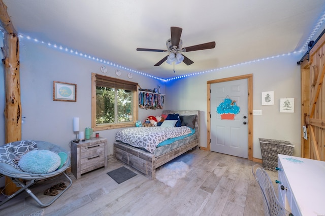 bedroom featuring a barn door, light wood-style flooring, and a ceiling fan