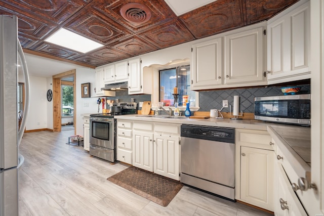 kitchen featuring an ornate ceiling, stainless steel appliances, light countertops, under cabinet range hood, and a sink