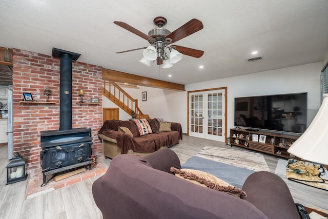 living area with a wood stove, light wood-style flooring, visible vents, and a textured ceiling