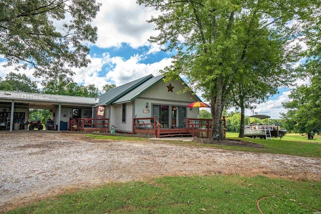 view of front facade with metal roof, an attached carport, driveway, a wooden deck, and a front lawn