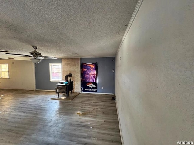 unfurnished living room featuring a wood stove, ceiling fan, a textured ceiling, and wood finished floors