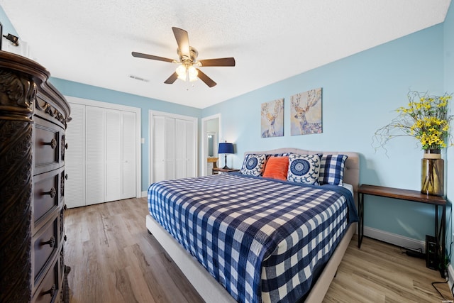 bedroom featuring visible vents, ceiling fan, a textured ceiling, light wood-type flooring, and multiple closets