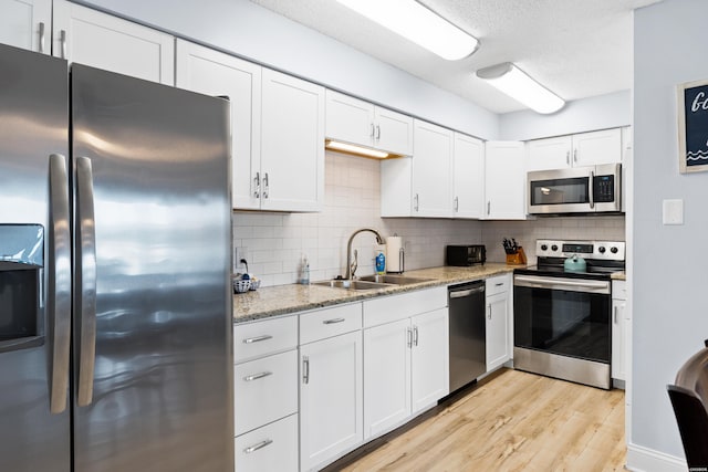 kitchen featuring light stone counters, appliances with stainless steel finishes, white cabinets, and a sink