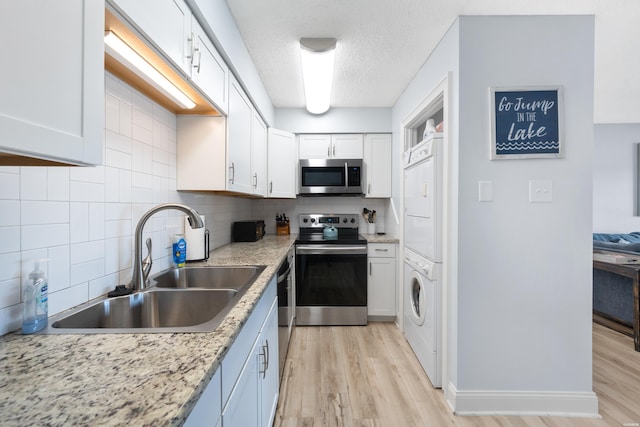 kitchen featuring appliances with stainless steel finishes, stacked washer / drying machine, white cabinetry, and a sink