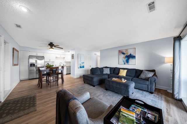 living room with a ceiling fan, a textured ceiling, visible vents, and wood finished floors