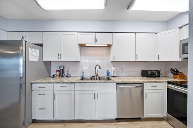 kitchen with light stone countertops, white cabinetry, appliances with stainless steel finishes, and a sink