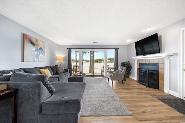 living area featuring baseboards, a textured ceiling, a tiled fireplace, and wood finished floors