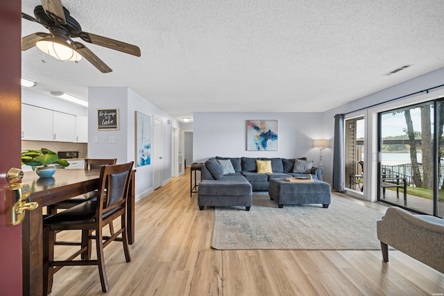 living room featuring a textured ceiling, light wood-type flooring, and a ceiling fan