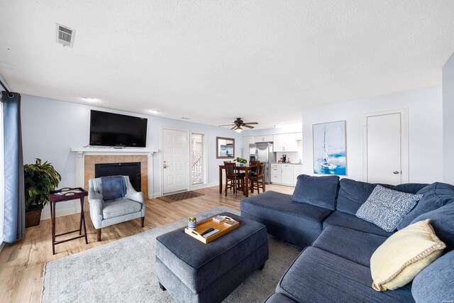 living area featuring a textured ceiling, a tile fireplace, light wood-style flooring, visible vents, and baseboards