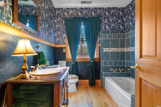 bathroom featuring a garden tub, visible vents, toilet, wood finished floors, and wallpapered walls