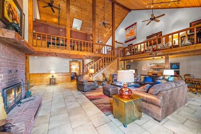 living room featuring wooden walls, a fireplace, a ceiling fan, wood ceiling, and stairs