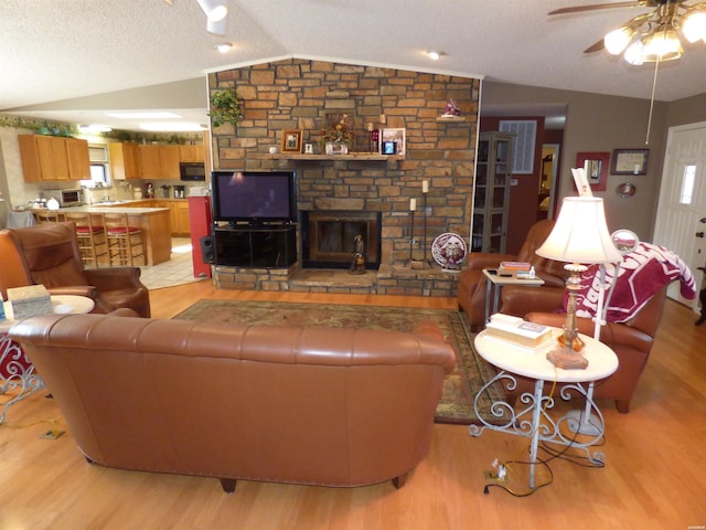 living area featuring lofted ceiling, ceiling fan, a textured ceiling, a fireplace, and light wood-type flooring