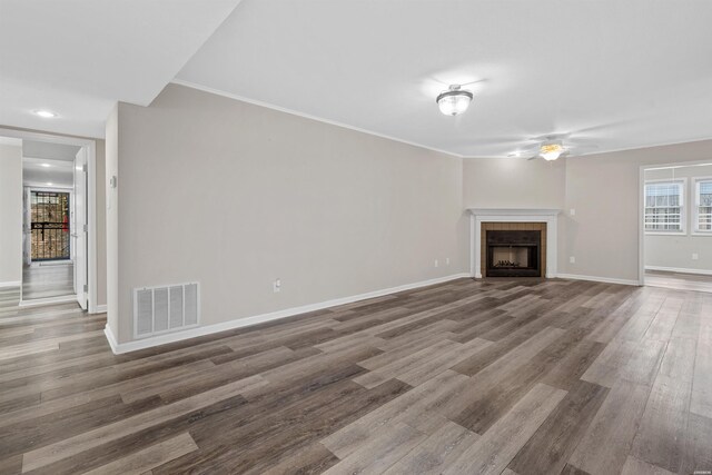 unfurnished living room with visible vents, a tiled fireplace, a ceiling fan, wood finished floors, and baseboards