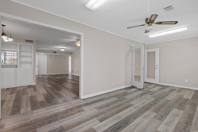 empty room with visible vents, wood finished floors, crown molding, and ceiling fan with notable chandelier