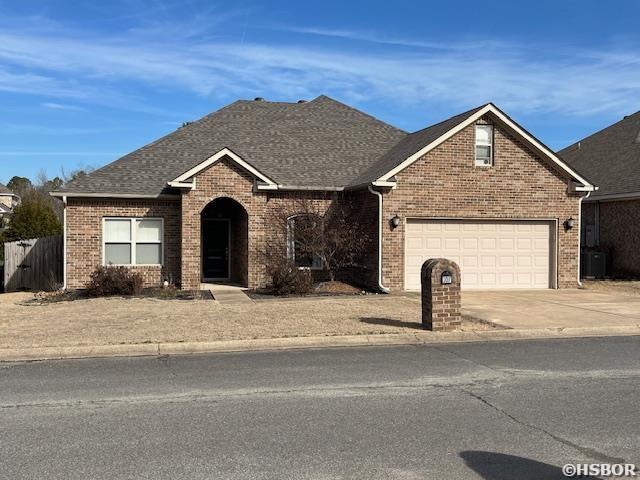 view of front of home featuring driveway, a garage, a shingled roof, cooling unit, and brick siding