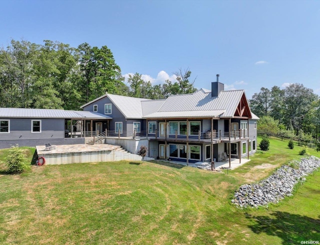 rear view of property with metal roof, a chimney, a patio, and a lawn