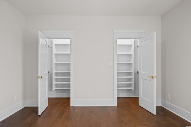 unfurnished bedroom featuring a spacious closet, dark wood-style flooring, a closet, and baseboards