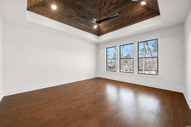empty room with a tray ceiling, dark wood finished floors, and baseboards