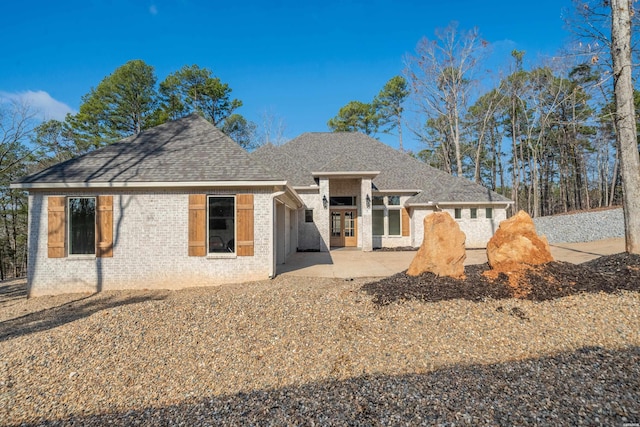 rear view of property featuring roof with shingles, a patio, and brick siding