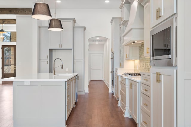 kitchen with a center island with sink, custom exhaust hood, light countertops, hanging light fixtures, and appliances with stainless steel finishes