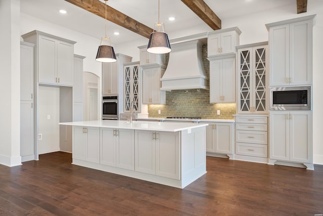 kitchen featuring pendant lighting, light countertops, appliances with stainless steel finishes, a kitchen island with sink, and premium range hood