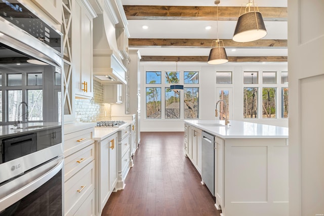 kitchen with light countertops, appliances with stainless steel finishes, a center island with sink, and decorative light fixtures