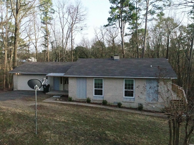 single story home featuring brick siding, a front yard, a chimney, a garage, and driveway