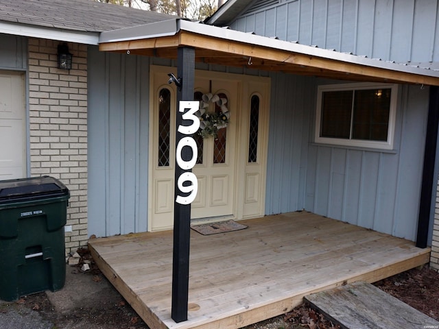 doorway to property featuring brick siding, board and batten siding, and roof with shingles