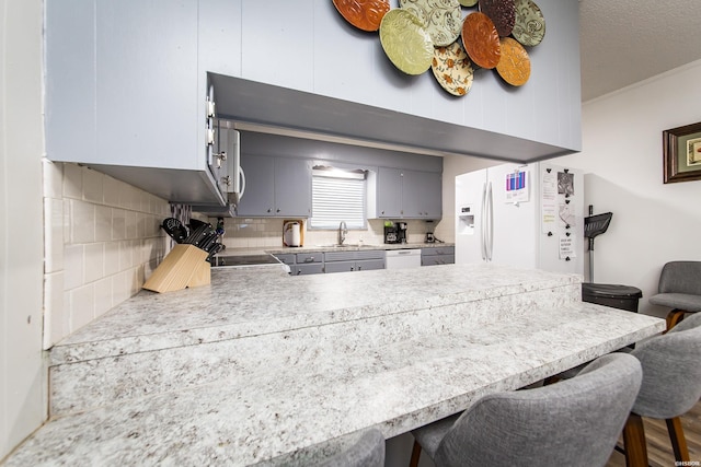 kitchen with a kitchen breakfast bar, a peninsula, a sink, light countertops, and backsplash