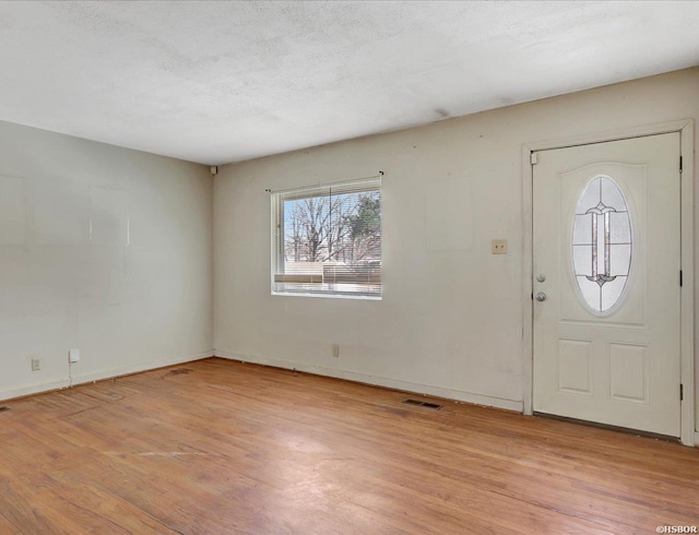 foyer entrance featuring a textured ceiling, light wood finished floors, visible vents, and baseboards