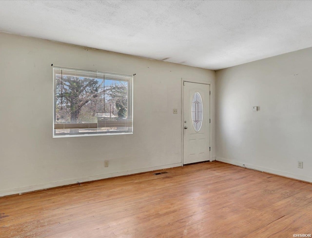 entryway featuring a textured ceiling, light wood finished floors, visible vents, and baseboards