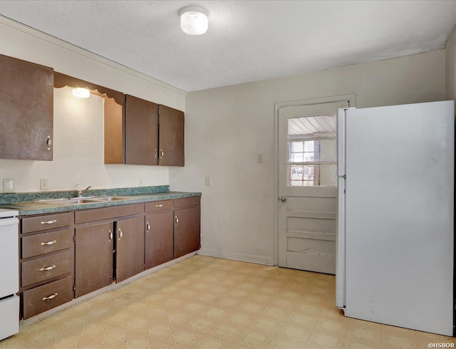 kitchen with a sink, dark brown cabinets, freestanding refrigerator, light floors, and dark countertops