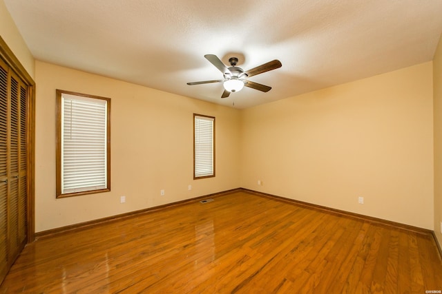unfurnished bedroom featuring ceiling fan, baseboards, wood finished floors, visible vents, and a closet