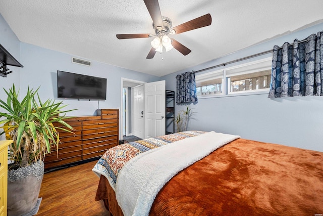 bedroom with a ceiling fan, visible vents, a textured ceiling, and wood finished floors