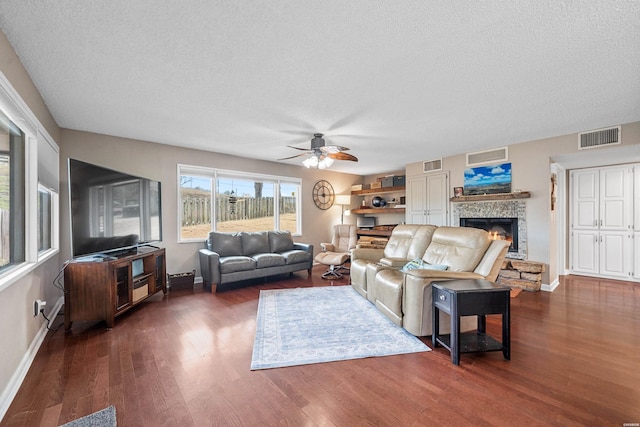 living area featuring visible vents, dark wood-type flooring, a stone fireplace, a textured ceiling, and baseboards