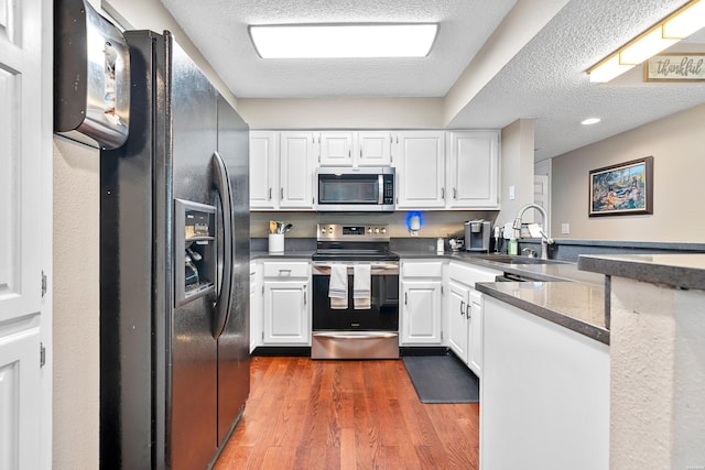 kitchen with stainless steel appliances, a peninsula, a sink, white cabinets, and dark wood-style floors