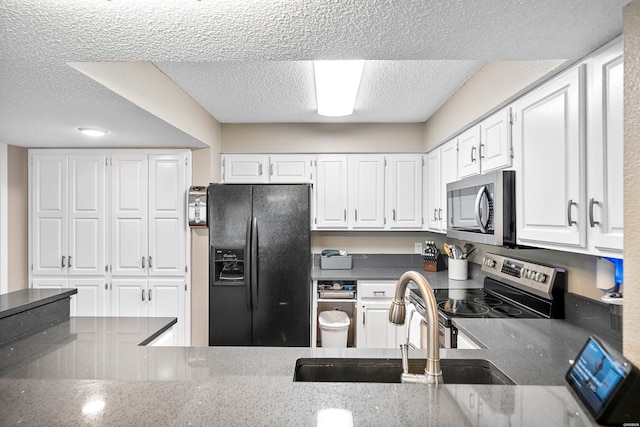 kitchen with white cabinets, dark countertops, appliances with stainless steel finishes, a textured ceiling, and a sink