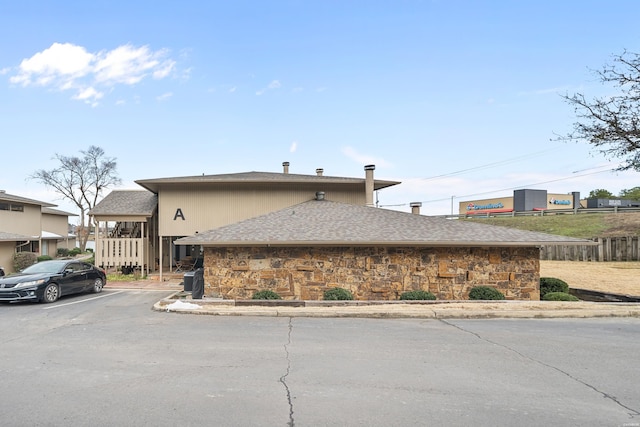 view of side of property featuring uncovered parking, stone siding, and roof with shingles