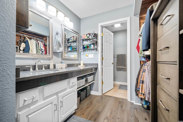 bathroom with a textured ceiling, wood finished floors, vanity, and baseboards