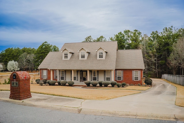 new england style home with brick siding, roof with shingles, and fence