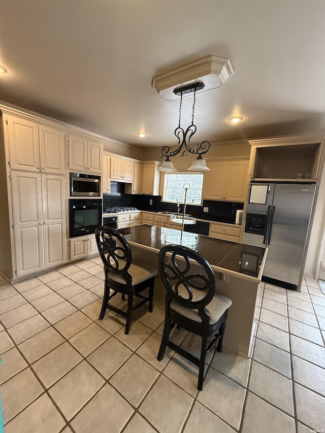 kitchen with pendant lighting, light tile patterned floors, dark countertops, cream cabinets, and appliances with stainless steel finishes