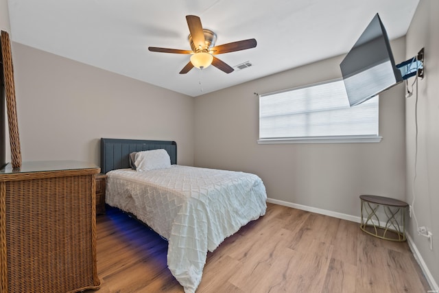 bedroom with a ceiling fan, visible vents, baseboards, and wood finished floors