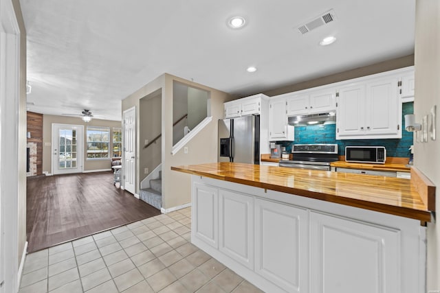 kitchen featuring appliances with stainless steel finishes, under cabinet range hood, visible vents, and wood counters