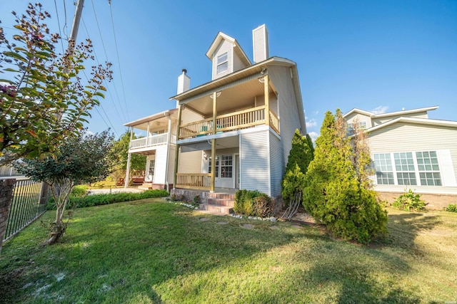 back of house with a porch, a balcony, fence, a lawn, and a chimney