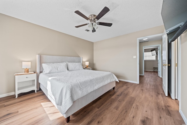 bedroom with a textured ceiling, ceiling fan, wood finished floors, visible vents, and baseboards