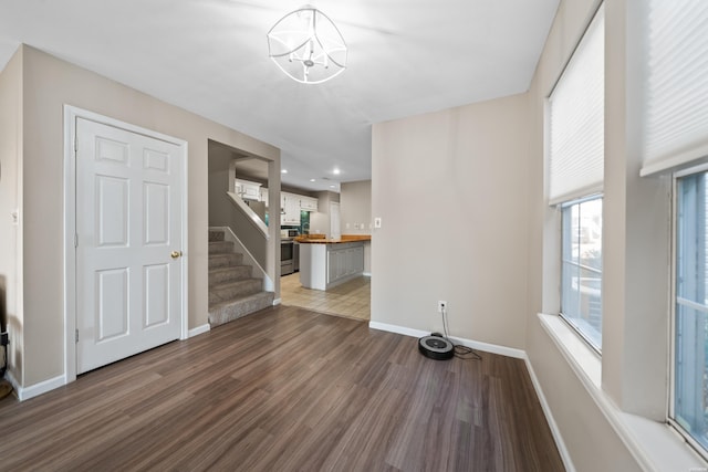 unfurnished living room with wood finished floors, a notable chandelier, baseboards, and stairs