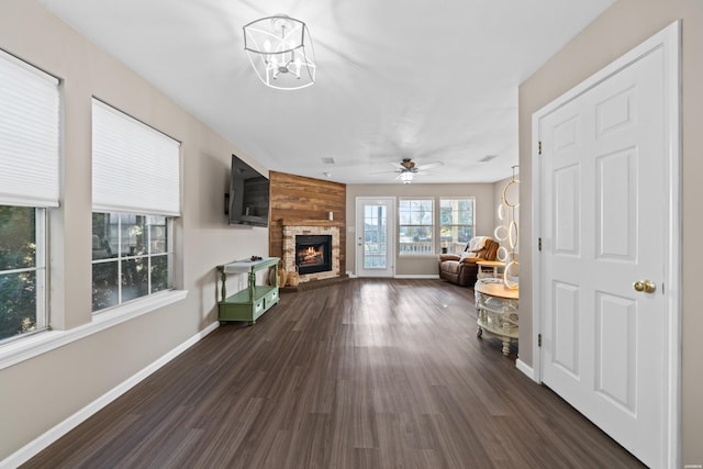 living area featuring dark wood-style floors, a lit fireplace, baseboards, and ceiling fan with notable chandelier